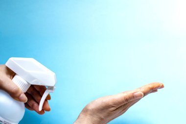 Bir kadın eline plastik sprey şişesinden antiseptik sıkar. Mavi arka planda yakın plan bir şişe ile eller. Salgın sırasında hijyenik tedavi.