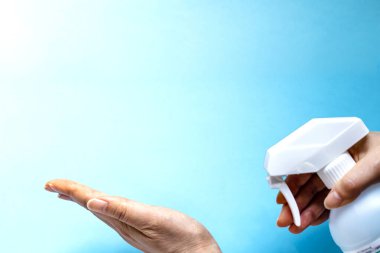 Bir kadın eline plastik sprey şişesinden antiseptik sıkar. Mavi arka planda yakın plan bir şişe ile eller. Salgın sırasında hijyenik tedavi.