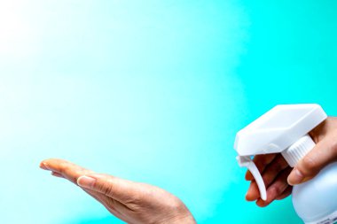 Bir kadın eline plastik sprey şişesinden antiseptik sıkar. Mavi yeşil arka plan üzerinde yakın plan bir şişe ile eller. Salgın sırasında hijyenik tedavi.