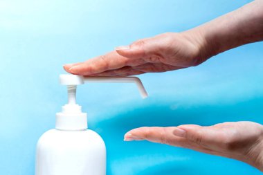 Bir kadın eline plastik sprey şişesinden antiseptik sıkar. Mavi arka planda yakın plan bir şişe ile eller. Salgın sırasında hijyenik tedavi.