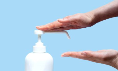 Bir kadın eline plastik sprey şişesinden antiseptik sıkar. Açık mavi arka planda yakın plan bir şişe ile eller. Salgın sırasında hijyenik tedavi.
