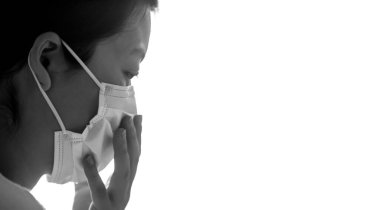 Genç bir kadın renk yüzeyine basit bir beyaz hava koruma maskesi takıyor. Grip, ateş, salgın, salgın belirtileri. Profil görünümü ve siyah ve beyaz.