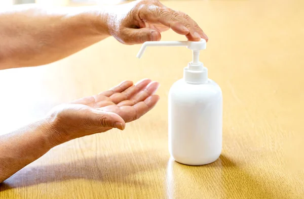 A senior man sprays hands with antiseptic from a plastic spray bottle. Hands with a bottle close-up on a wooden background. Sanitary treatment during an epidemic.