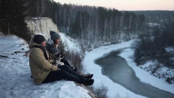 La joven familia se sienta en una ladera de invierno en el río. Amor en familia — Vídeos de Stock