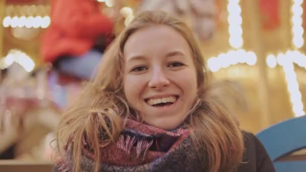 Mooie jonge vrouw lacht en glimlacht, carrousel op de achtergrond — Stockvideo