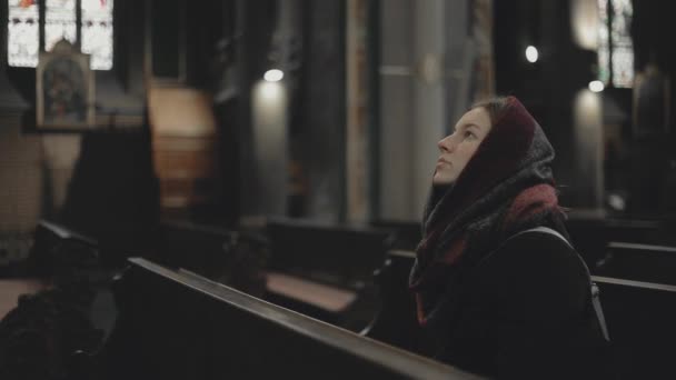 Jovem mulher senta-se na igreja católica. Menina turística na catedral: dentro do lugar santo — Vídeo de Stock