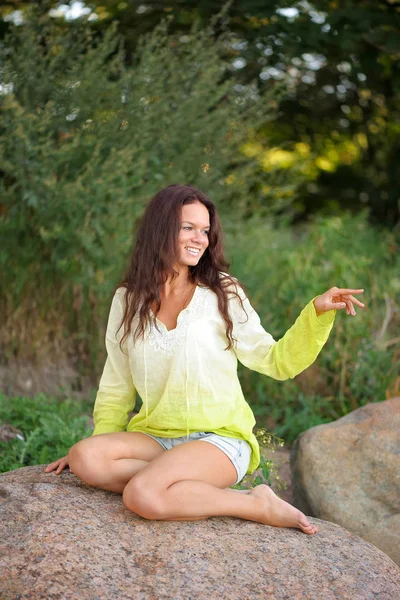 Mulher sorridente sentar-se sobre as pedras — Fotografia de Stock