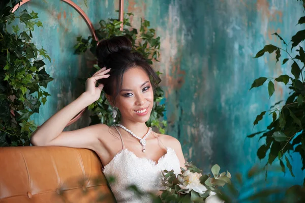 Sposa asiatica con fiori in abito bianco seduta sul divano — Foto Stock