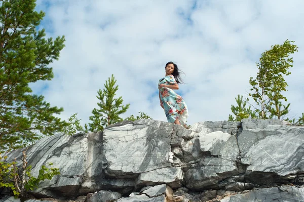 Νεαρή γυναίκα με μακρύ φόρεμα ποζάρει σε μαρμάρινο βράχο — Φωτογραφία Αρχείου