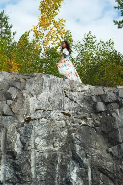 Νεαρή γυναίκα με μακρύ φόρεμα ποζάρει σε μαρμάρινο βράχο — Φωτογραφία Αρχείου