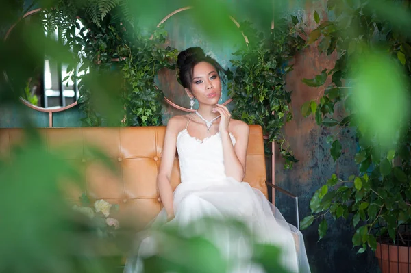 Noiva asiática com flores em vestido branco sentado no sofá — Fotografia de Stock