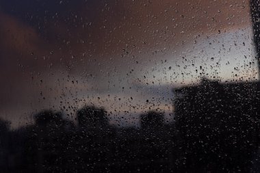 Penceredeki yağmur damlaları alacakaranlık şehrinin arka planına karşı
