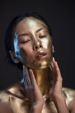 Stüdyoda siyah arka planda altın boyalı genç Asyalı kadın portresi.