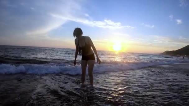 Молода жінка втратила щось у морській воді і йде до моря. Повільний силует руху — стокове відео