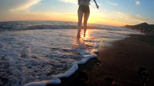 Ung kvinna springer och händerna upp på gyllene solnedgång bakgrund vid sandstrand i havsvågor. Slow motion siluett — Stockvideo