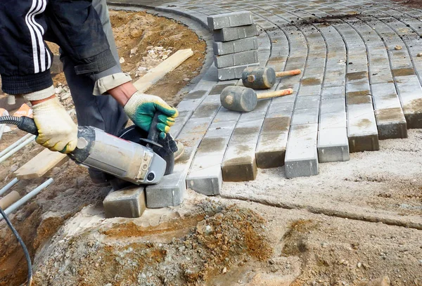 En man sågar en elektrisk såg med en stenläggning platta, reparera en sten sökväg. — Stockfoto
