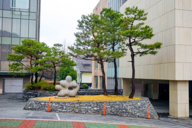 Seul, Mart - 2019: Küçük mimari formlar. Taş soyutlama ve yeşil çam ağaçları. Ofis binaları.