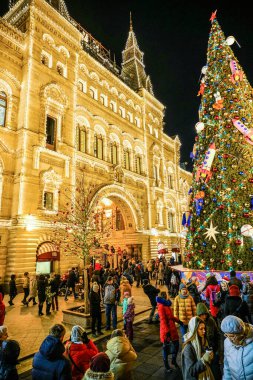 Moskova - Aralık 2019: İnsanlar şenlikli bir cadde boyunca yürüyor. Noel oyuncaklarıyla Noel ağacı. Sakız binası elektrikli çelenklerle süslenmiş..