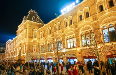 Moskova - Aralık 2019: İnsanlar şenlikli bir cadde boyunca yürüyor. Noel oyuncaklarıyla Noel ağacı. Sakız binası elektrikli çelenklerle süslenmiş..