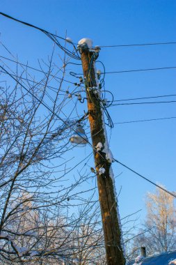 Kablolu elektrik direği, mavi gökyüzü. Karda ağaç dalları, direkte bir fener..