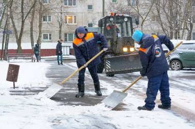 Workers in uniform with big shovels, a tractor removes snow from the road. Snow removal on the city streets.