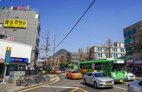 Cruzamento ocupado com tráfego pesado de carros e ônibus. Dia ensolarado, céu azul, casas com sinais brilhantes . — Fotografia de Stock