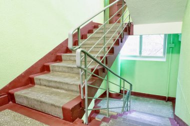 Bir apartmanın içinde çöp kanalı olan merdiven, duvarlar parlak yeşil boya ve pencerenin ışığıyla boyanmış..