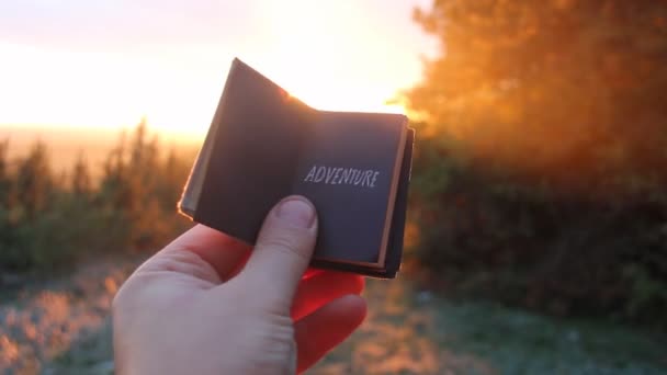 Idea avventura. Viaggiatore che tiene un libro con l'iscrizione e il tramonto — Video Stock