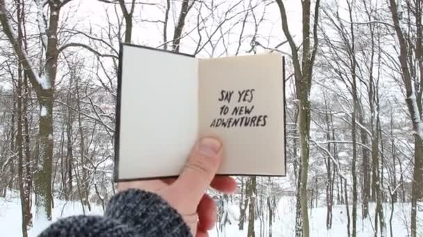 Hombre sosteniendo un libro con la inscripción Di sí a nuevas aventuras en el fondo del bosque de invierno — Vídeos de Stock