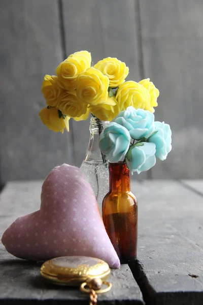 Kwiaty w butelkach na vintage tabeli z sercem. — Zdjęcie stockowe