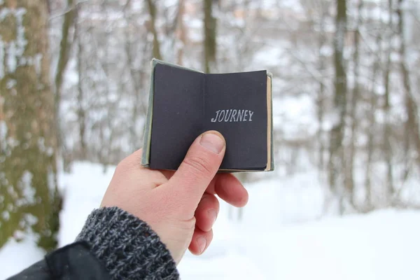 Joyrney idé. Handen håller en bok med inskriptionen. På bakgrund av skogen snörik vinter — Stockfoto