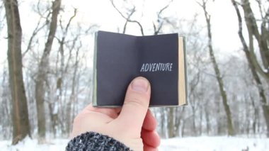 Macera, metin bir kitapla karlı kış orman arka plan üzerinde tutan erkek