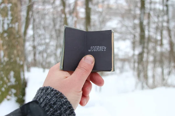 Joyrney koncept. Handen håller en bok med inskriptionen. På bakgrund av skogen vinter — Stockfoto