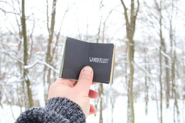 Handen håller en bok med den inskrift reslust på bakgrunden av skogen vinter — Stockfoto