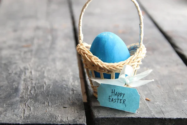 Frohe Ostern. blaues Ei auf rustikalem Tisch und ein Korb mit Anhänger. — Stockfoto