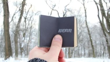 Macera, metin bir kitapla karlı kış park arka plan üzerinde tutan el