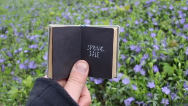 Frühjahrsverkauf Idee, Buch mit Text und Frühlingsfeld mit blauen Blumen — Stockvideo