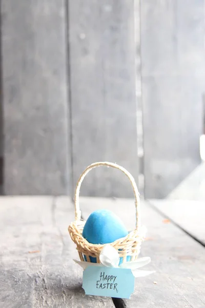 Feliz Pascua. Huevo azul sobre mesa rústica y canasta con etiqueta . — Foto de Stock