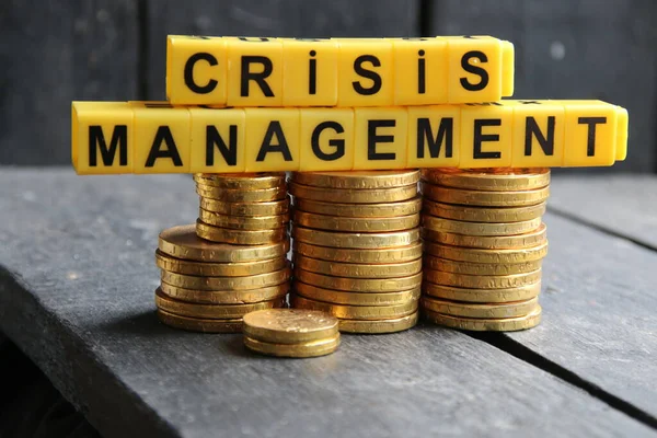 Crisis Management - yellow cubes inscription and a stack of gold coins, creative concept.