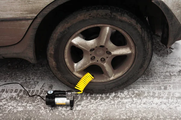Kışın elektrikli pompayla araba tekerleğini şişirmek, yakın plan.