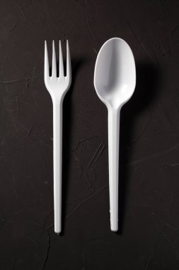Tek kullanımlık çatal ve kaşık koyu bir arka planda.