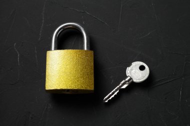 Anahtarı olan asma kilit koyu bir arkaplanda yatıyor
