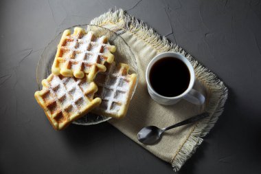 Şeffaf tabakta ev yapımı waffle 'lar ve ışıklı bir masada kahve fincanı.