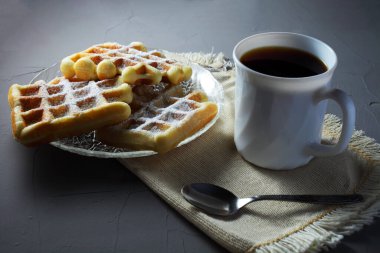 Şeffaf tabakta ev yapımı waffle 'lar ve ışıklı bir masada kahve fincanı.