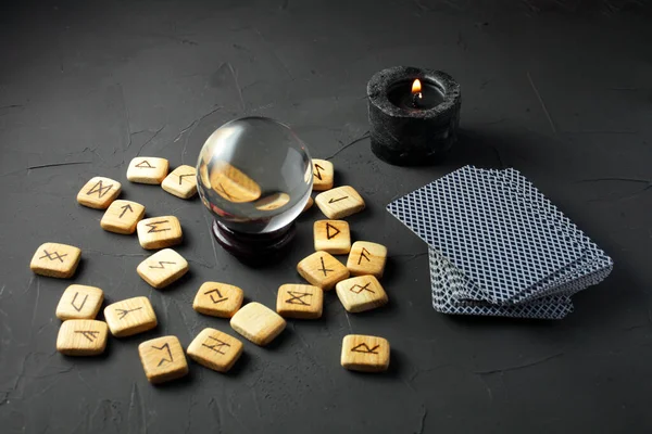 magic runes, crystal ball, cards and a black candle on a dark table