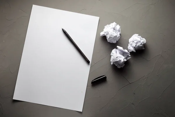 blank white paper, pen for writing and three crumpled sheets of paper on concrete background