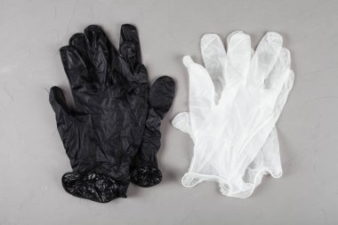 Gri arka planda tek kullanımlık beyaz ve siyah eldivenler.