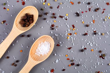 Ahşap kaşıklar, biber ve deniz tuzu ile gri arka planda.