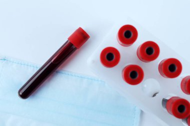 Tıbbi bir maskeye yakın kan taşıyan vakum test tüpleri, tonlu mavi, yumuşak odaklı.