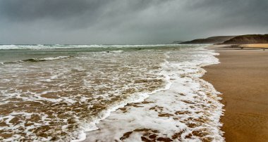 Brittany 'de kışın kumsalda. Okyanus dalgalarının beyaz köpüğü yağmurla dolu karanlık bir gökyüzünün altında ölmek için gelir..